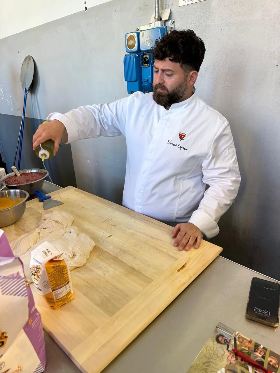 Il pizzaiolo aggiunge il condimento al banco di lavoro.