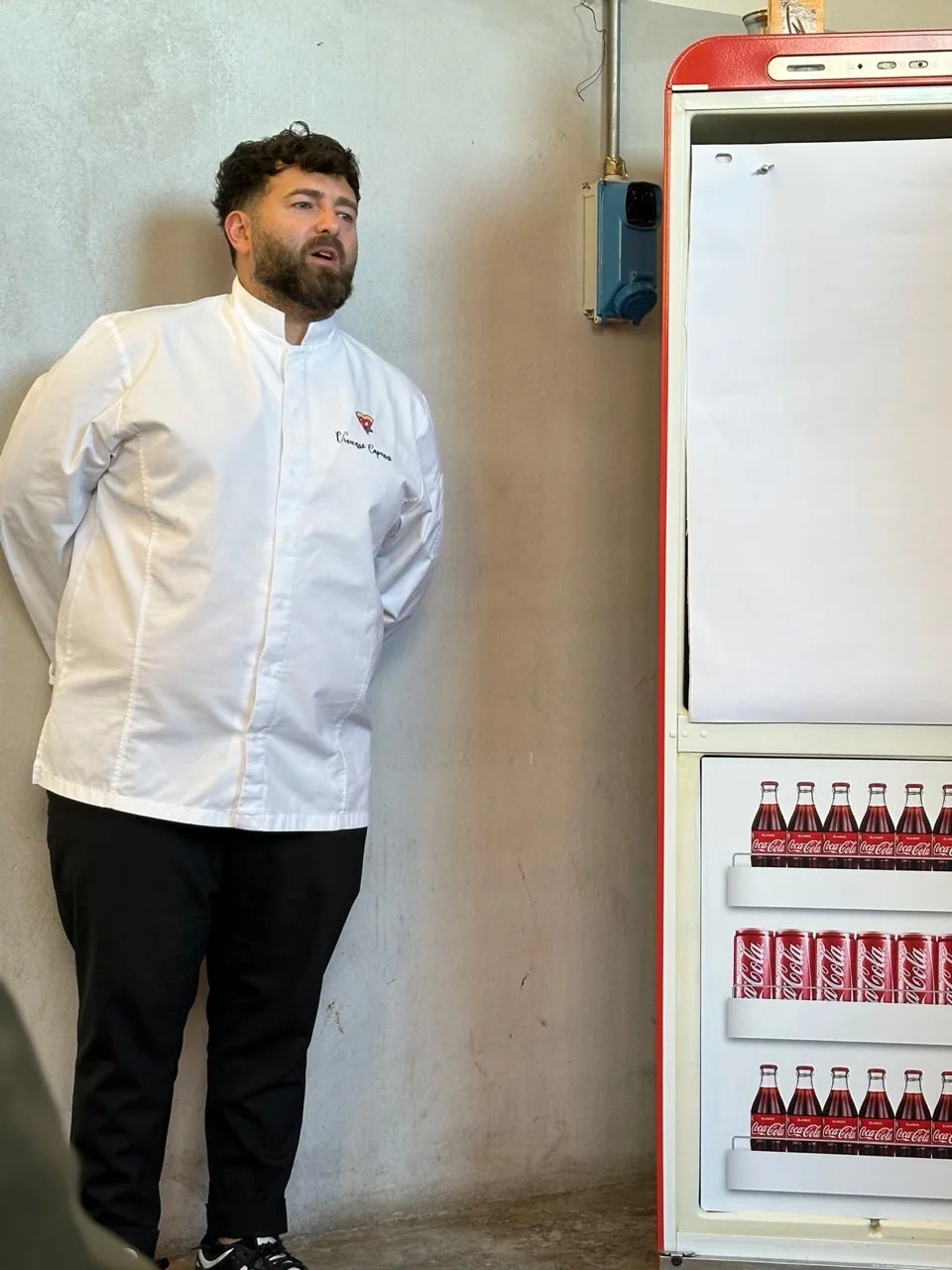 Il pizzaiolo accanto al frigorifero delle bevande nel locale.